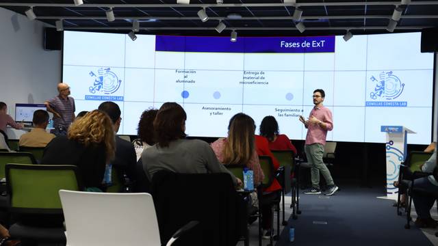 Una presentación en una sala de conferencia donde dos ponentes destacan las fases de un proyecto frente a una audiencia.