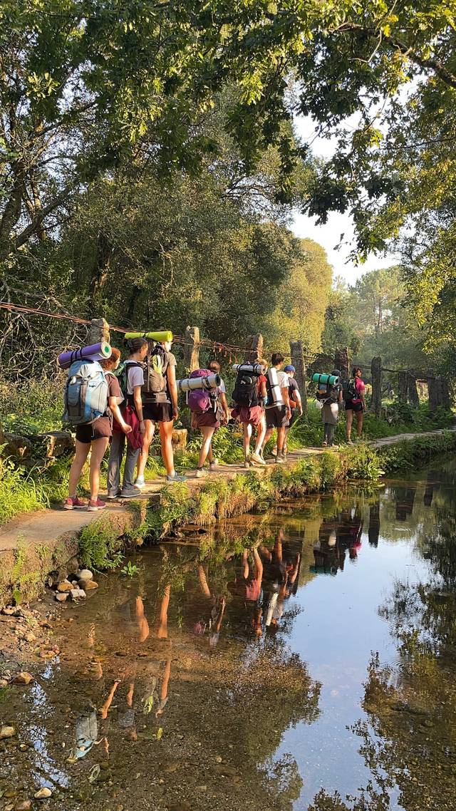 Un grupo de personas camina por un sendero junto a un río en un entorno natural.