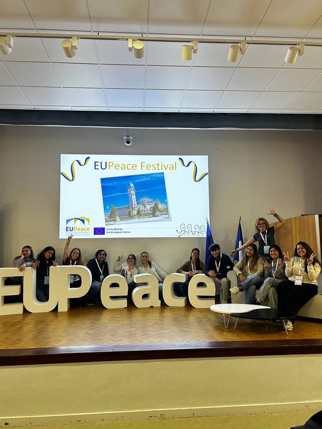 Un grupo de personas participa en el festival EUPeace, posando con un gran letrero de la palabra 'EUPeace'.