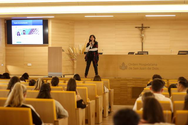 Una mujer presenta un tema frente a un público sentado en un auditorio.