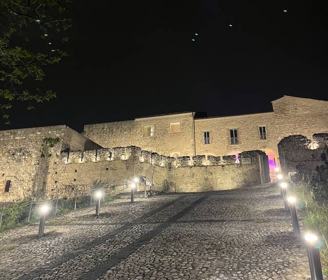 Un antiguo castillo iluminado por luces nocturnas en un camino de piedras.