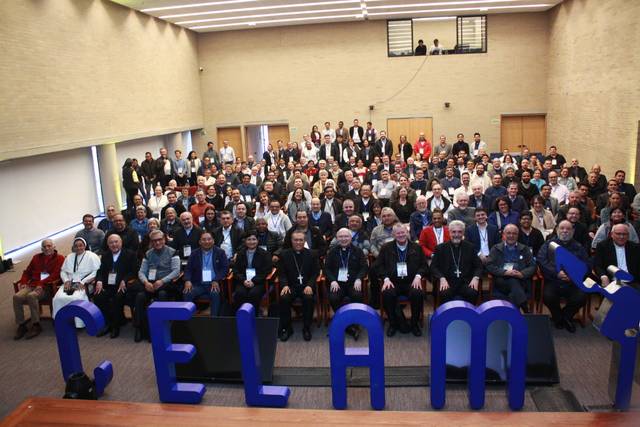 A large group of people posing for a photo in a conference room with the letters 'CELAM' in the foreground.