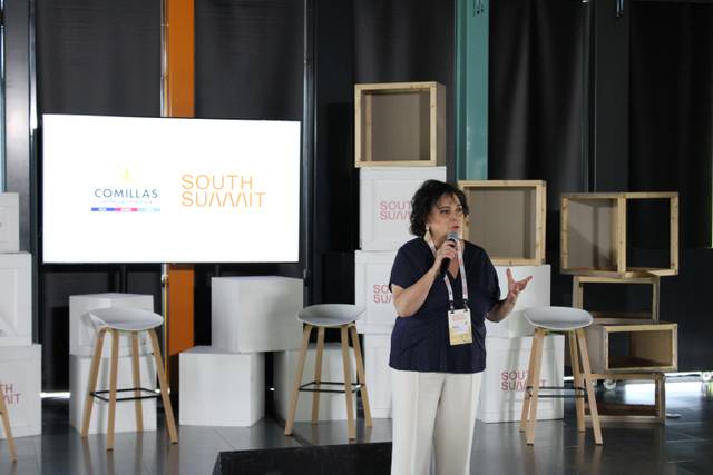 A woman is presenting at a conference with logos 'Comillas' and 'South Summit' visible in the background.