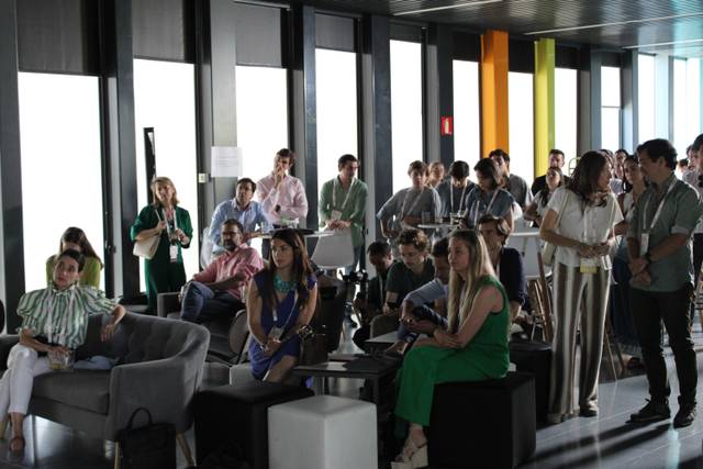 A group of people gathered in a modern office or conference space, listening intently to a presentation or speaker out of view.