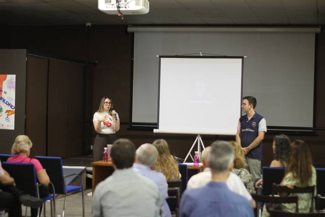 Una presentación en un evento con una mujer y un hombre frente a una audiencia sentada.