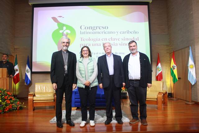 Four individuals posing in front of a presentation screen at a conference about Latin American theology.
