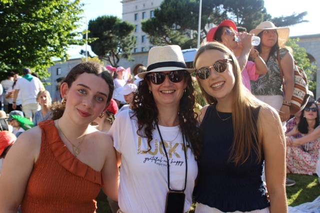 Tres mujeres posan sonrientes durante un evento al aire libre en un ambiente soleado.
