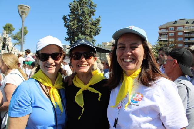 Tres mujeres sonrientes posan juntas con pañuelos amarillos al cuello en un evento al aire libre.