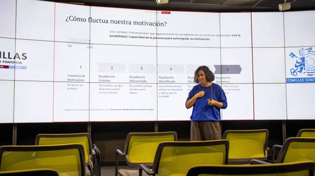 Una persona presenta en una sala con pantallas grandes que muestran un gráfico sobre la fluctuación de la motivación.
