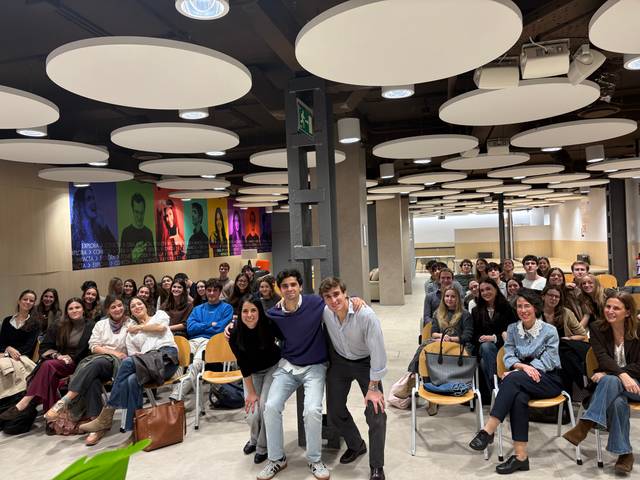 Un grupo grande de personas sonrientes posando en un salón con techo de lámparas redondas.