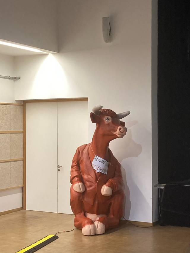 Una escultura de una vaca sentada con un abrigo en un escenario vacío.