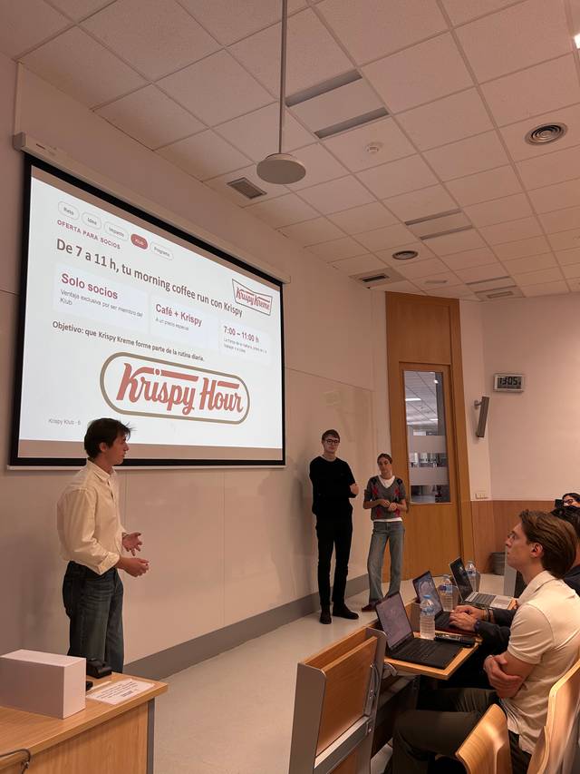 Un grupo de personas en una sala de clases escucha una presentación sobre una promoción de café llamada Krispy Hour.