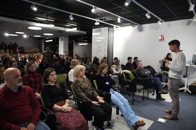 Un hombre joven está dando una presentación frente a un grupo de personas sentadas en una sala de conferencias.