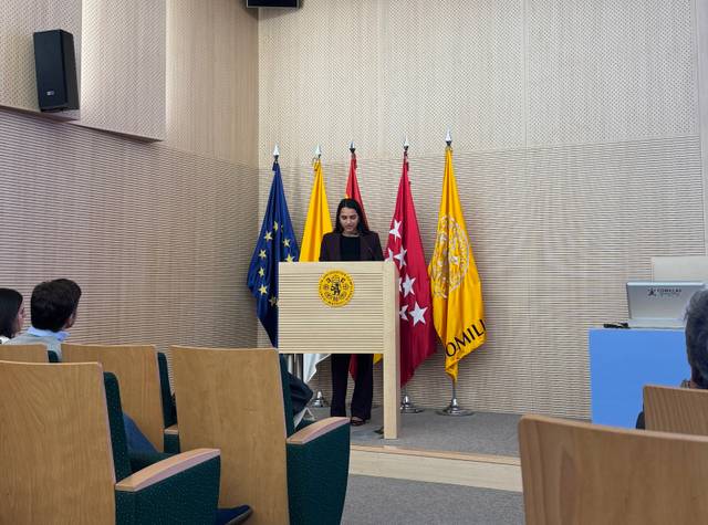 Una mujer está hablando en un atril frente a varias banderas en un auditorio.