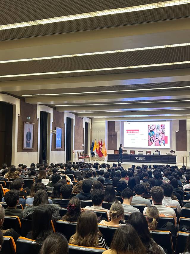 Una conferencia en un auditorio lleno de personas, con una presentación proyectada en una pantalla.
