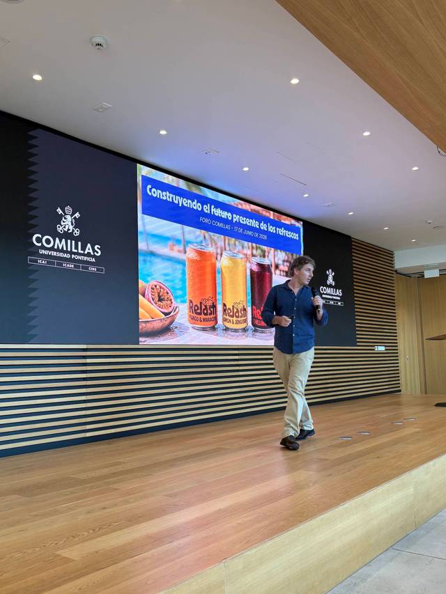 Un presentador habla sobre el futuro de los restaurantes en una conferencia con una pantalla de fondo que muestra bebidas.