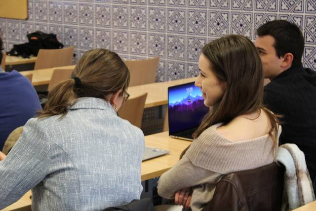 Dos personas conversan en un aula con un fondo decorado con azulejos.