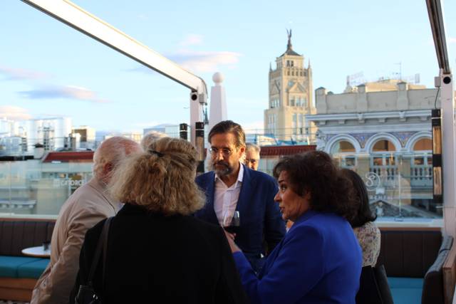 A group of people having a discussion on a rooftop with a historic building in the background.