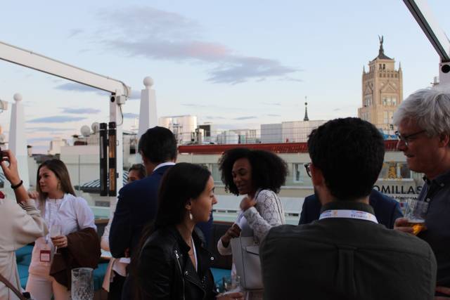 People socializing on a rooftop with a city view in the background during evening.