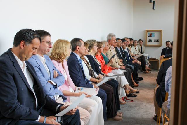 Un grupo de personas sentadas en una sala, mirando hacia adelante y sosteniendo documentos en sus manos.