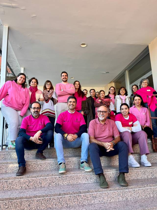 Un grupo de personas vestidas con camisetas rosas posando en unas escaleras.