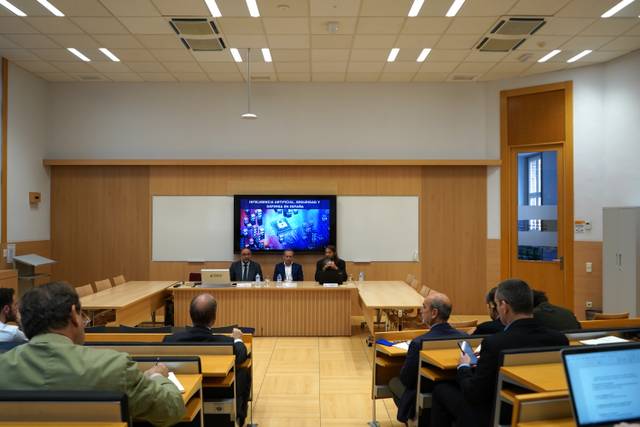Una reunión en un aula moderna con un panel de ponentes frente a una audiencia.