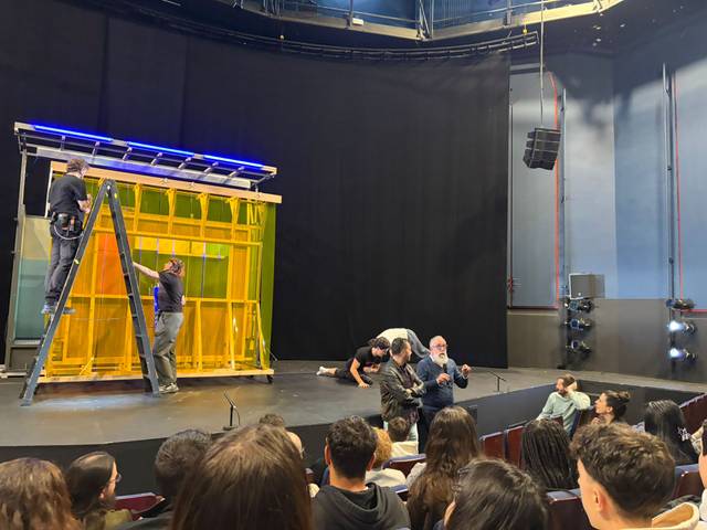 Un grupo de personas trabaja en un escenario mientras otros observan desde la audiencia.