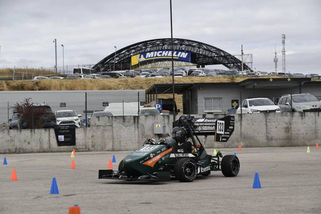 Un coche de carreras tipo fórmula realizando una prueba en un circuito marcado con conos de colores.