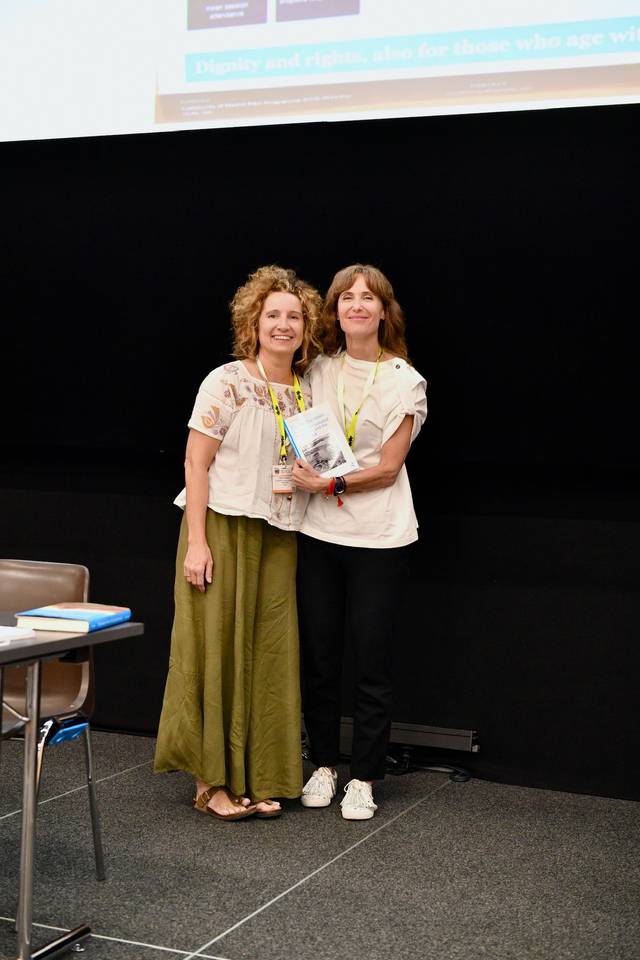 Dos mujeres se están tomando una foto juntas mientras sostienen un libro en un evento.