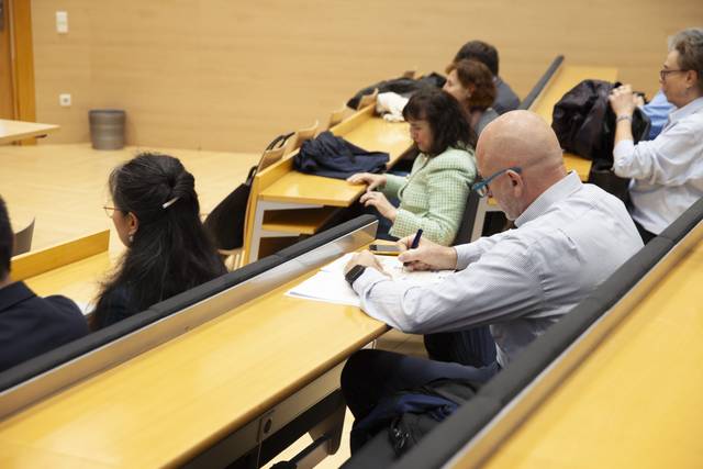 Un grupo de personas sentadas en un aula, algunas tomando notas y otras conversando.
