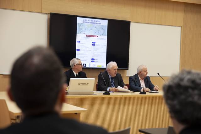 Un grupo de tres hombres mayores discute frente a una pantalla en una sala de conferencias.
