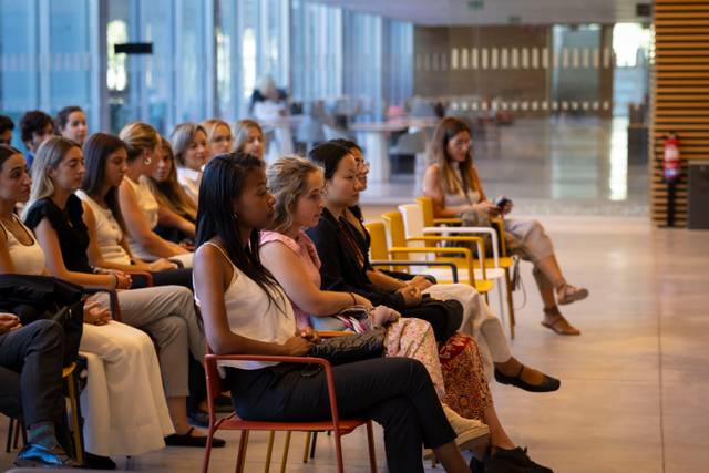 Un grupo de mujeres sentadas en sillas, prestando atención en un evento.