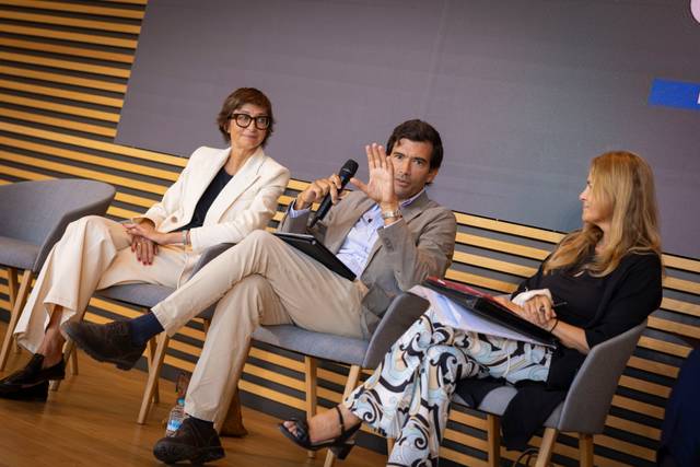 Un panel de discusión con tres personas sentadas, una de ellas hablando con un micrófono.