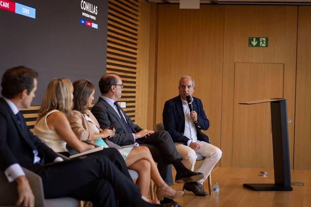 Un grupo de personas discutiendo en un panel durante un evento en un auditorio moderno.