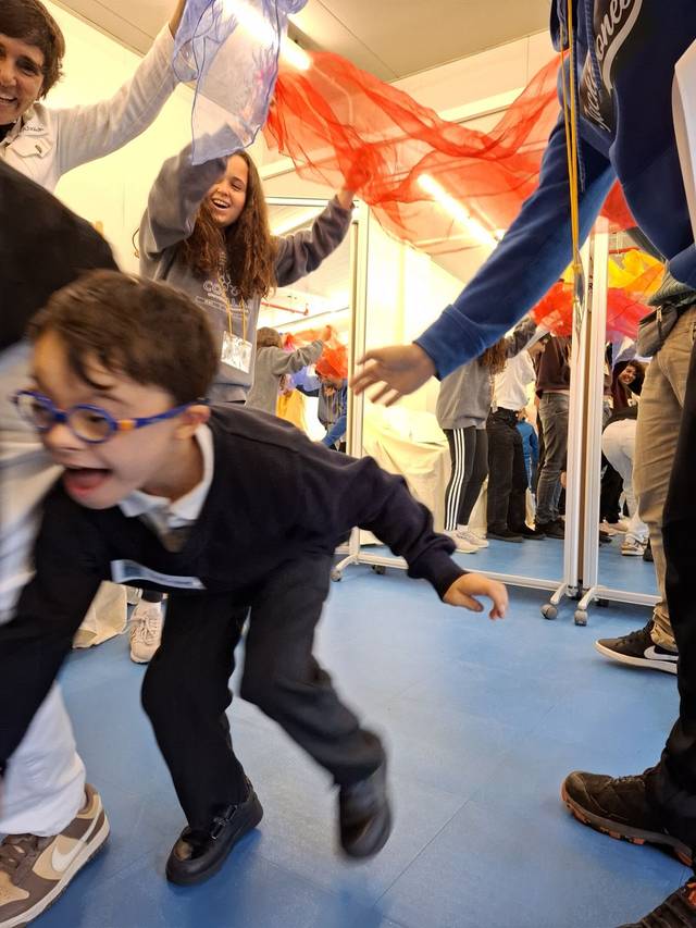 Un grupo de niños juega y ríe en un espacio cerrado mientras sostienen telas de colores.