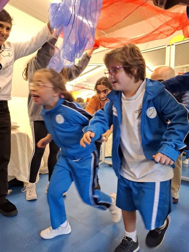 Un grupo de niños jugando y corriendo bajo telas de colores en un ambiente festivo.