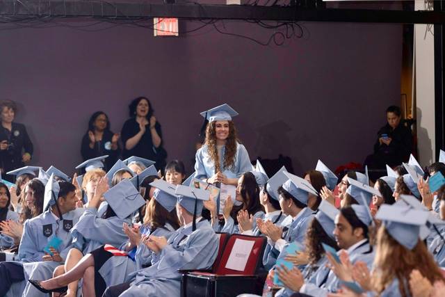 Una graduada sonriente recibe aplausos en una ceremonia de graduación.