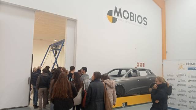 Un grupo de personas se encuentra frente a un coche expuesto en un evento de tecnología en un entorno industrial.