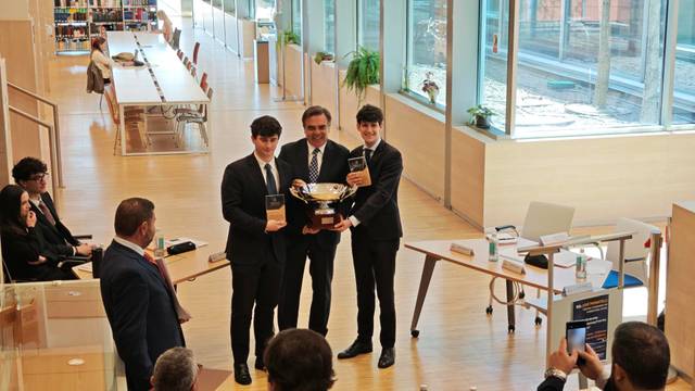 Dos jóvenes sonrientes sostienen un trofeo en un evento de premiación mientras un hombre los acompaña.