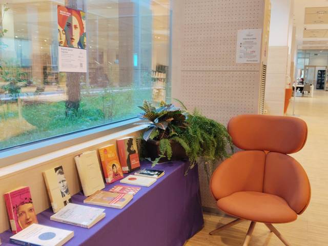 Un rincón acogedor de una biblioteca con una silla moderna y libros expuestos sobre una mesa.