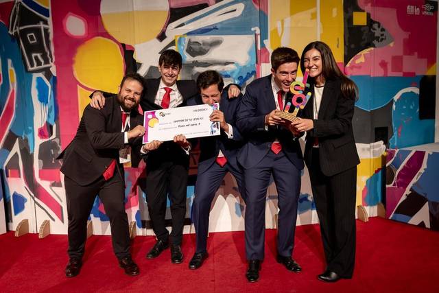 Un grupo de cinco personas sonrientes posan en un evento celebrando con un premio en la mano.