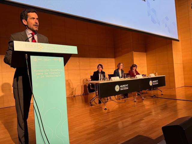 Un hombre habla en un podio frente a un panel de cuatro mujeres sentadas en una conferencia.