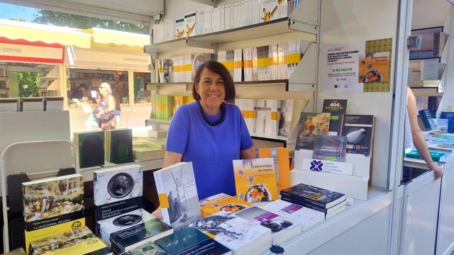 Belén Recio Godoy, Directora de Publicaciones de Comillas está de pie detrás de un mostrador lleno de libros en una feria.