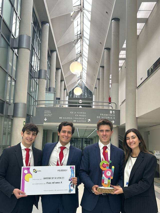 Grupo de cuatro personas vestidas formalmente en un edificio moderno sosteniendo un trofeo y un cartel.