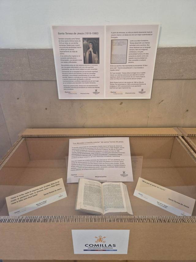 Exposición sobre Santa Teresa de Jesús con información sobre su vida y obras, junto a un libro abierto en una caja de cartón.