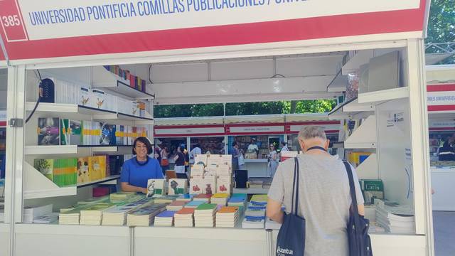 Un puesto de libros de la Universidad Pontificia Comillas en una feria con visitantes.