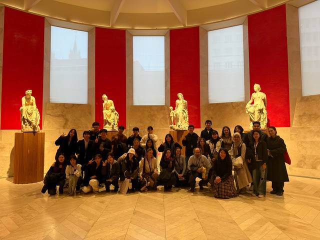 Un grupo de personas posando en una sala con estatuas y paredes rojas.