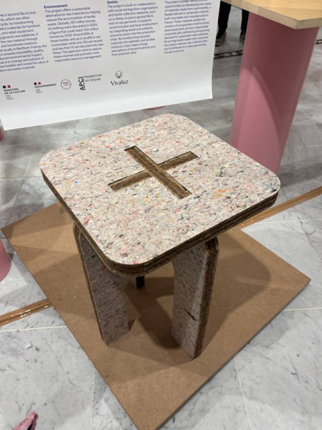 Una mesa pequeña de diseño minimalista fabricada con material reciclado y con un diseño de cruz en la superficie.