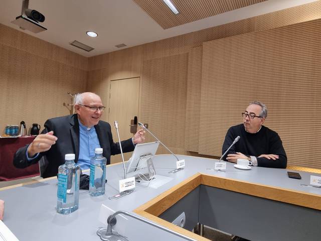 Two men engaging in a discussion at a conference table, with one gesturing while speaking.