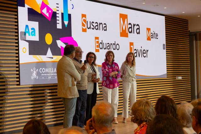 A group of people on a stage presenting at an event, with names projected in the background.